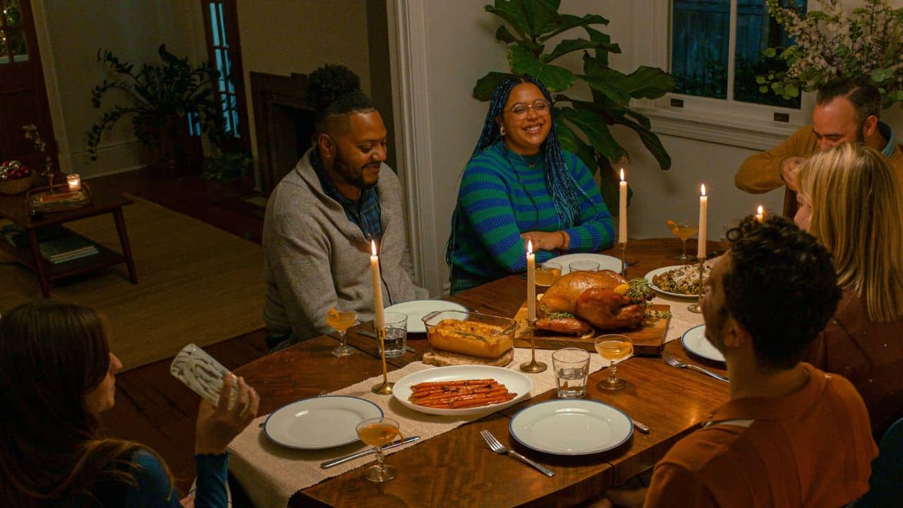A diverse group of friends or family are having a candlelit dinner, with a roasted turkey on the table.