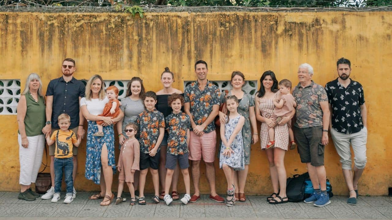 A large family stands together for a group photo in front of a yellow wall.