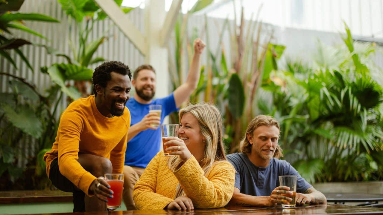 A group of four diverse friends are laughing and drinking together.