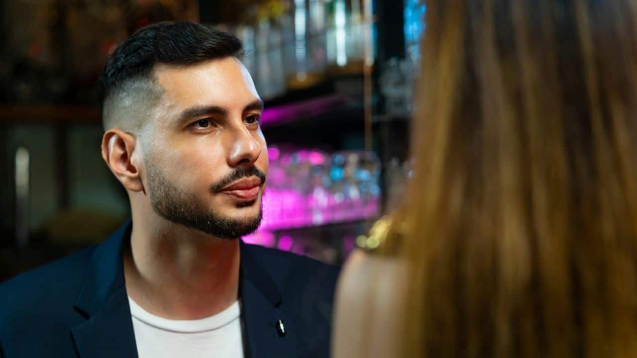 A man with a beard and dark hair looks at a woman with long hair.