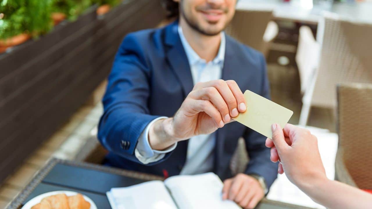A man in a suit hands a credit card to an unseen person.