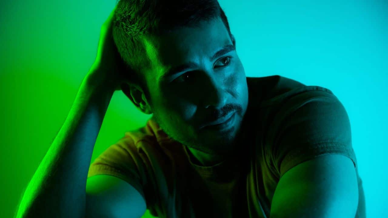 A man in a yellow shirt looks to the side, with his hand on his head.