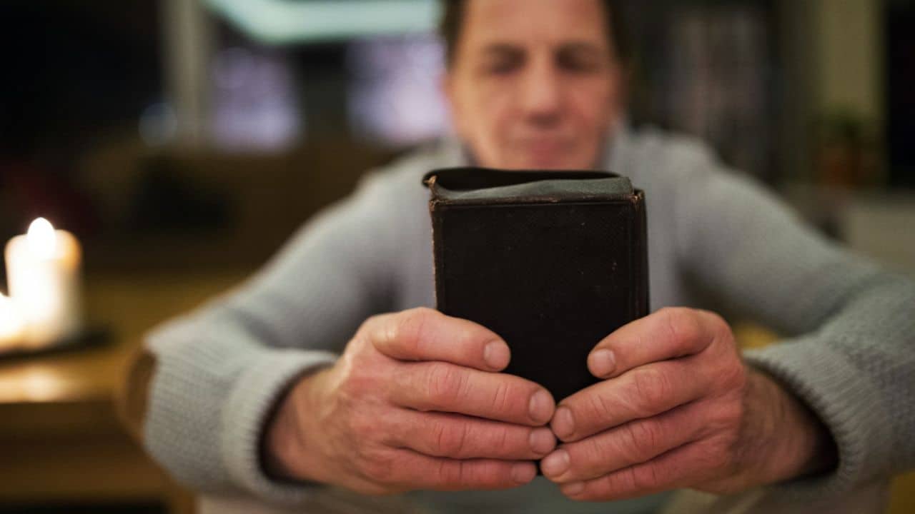 A man holds his phone in both hands, looking at it with a blurry background.