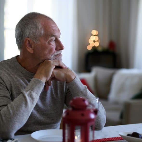 A contemplative older man with a beard sits at a dining table.