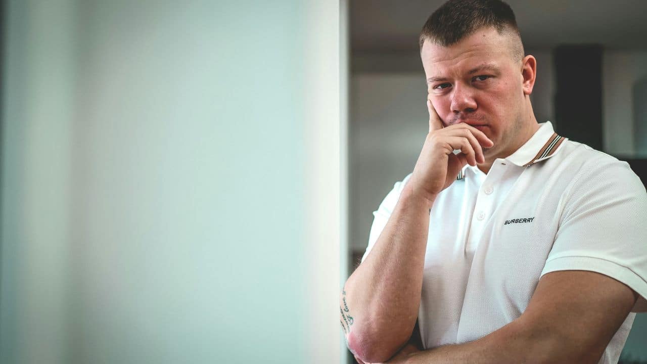 A serious man in a white polo shirt with a furrowed brow is looking at the camera.