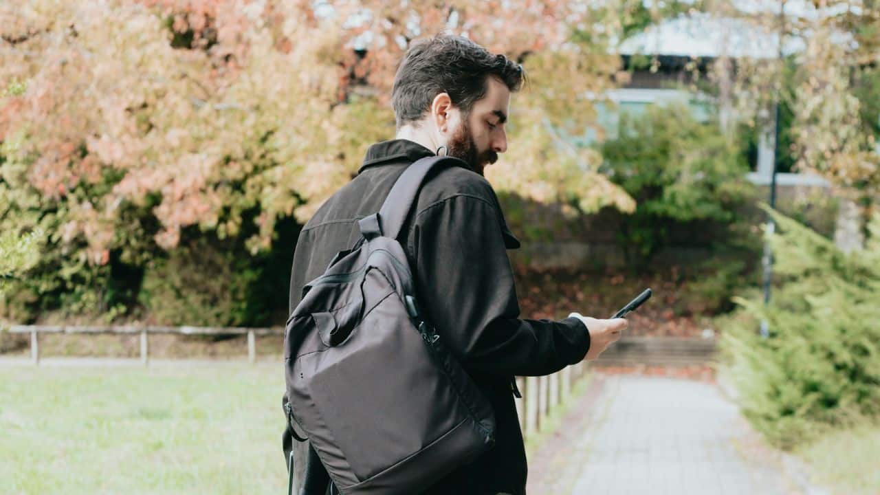 A man with a backpack is walking while looking at his phone.