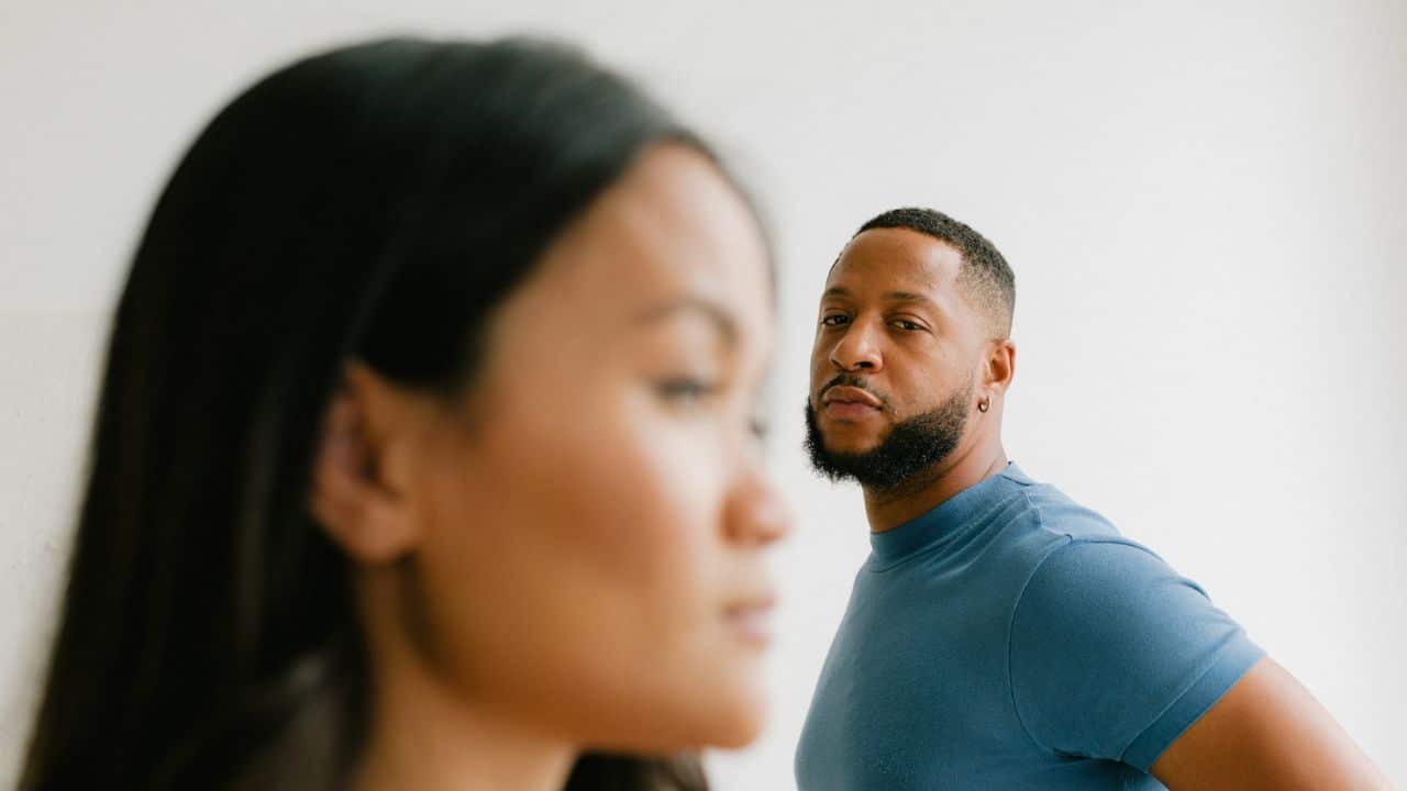 A bearded man is giving a serious stare at a woman in the foreground.