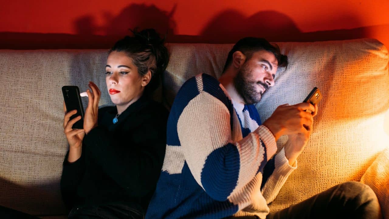 A man and a woman sit on a couch, looking at their phones.
