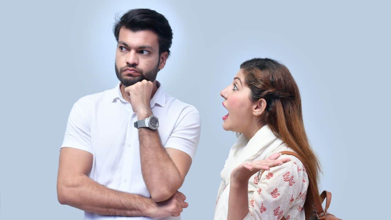 A bored-looking man listens to an exasperated woman gesturing and talking.