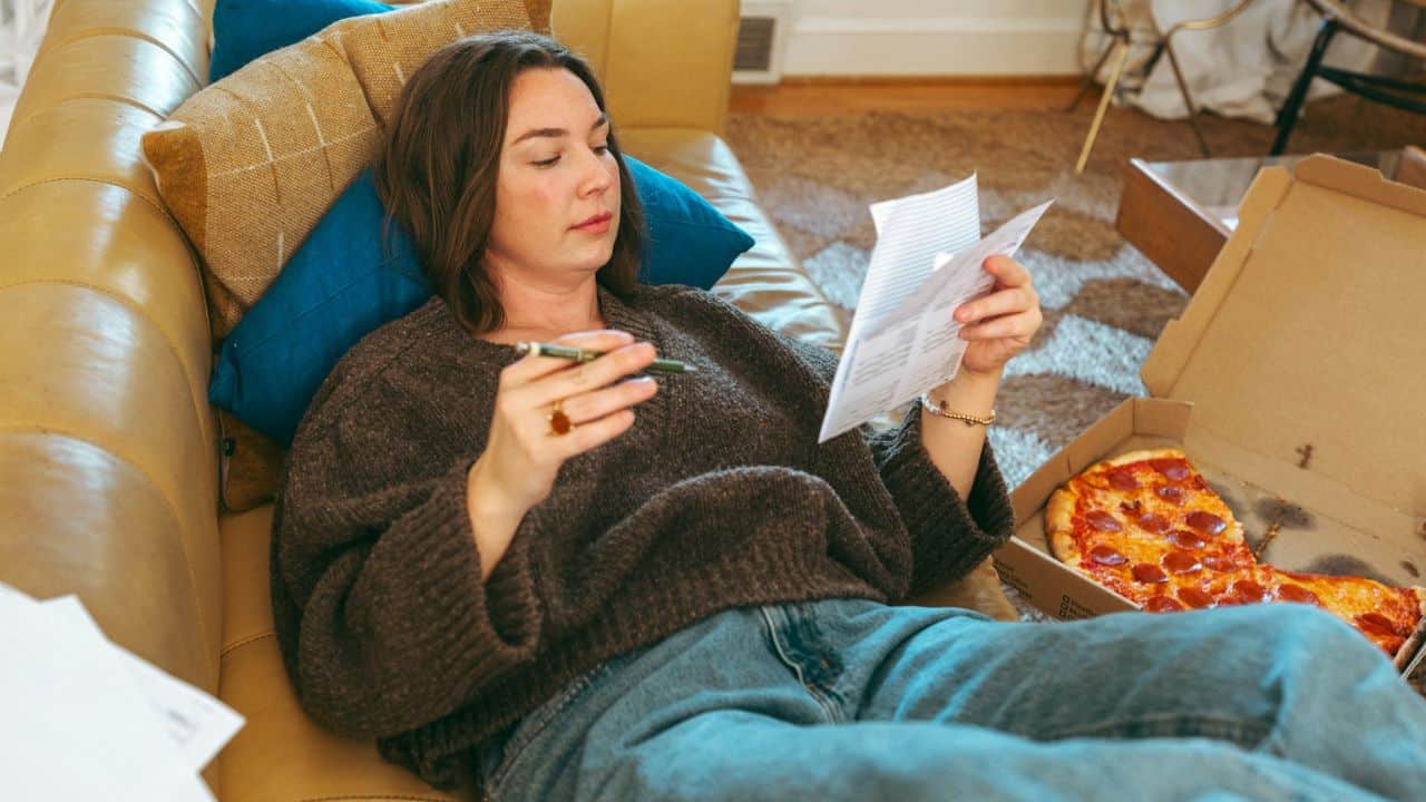 A man in a plaid shirt sits with his hand on his head, looking down.
