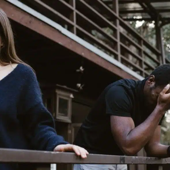 A distressed couple, a woman and a man, stand on a balcony outdoors.