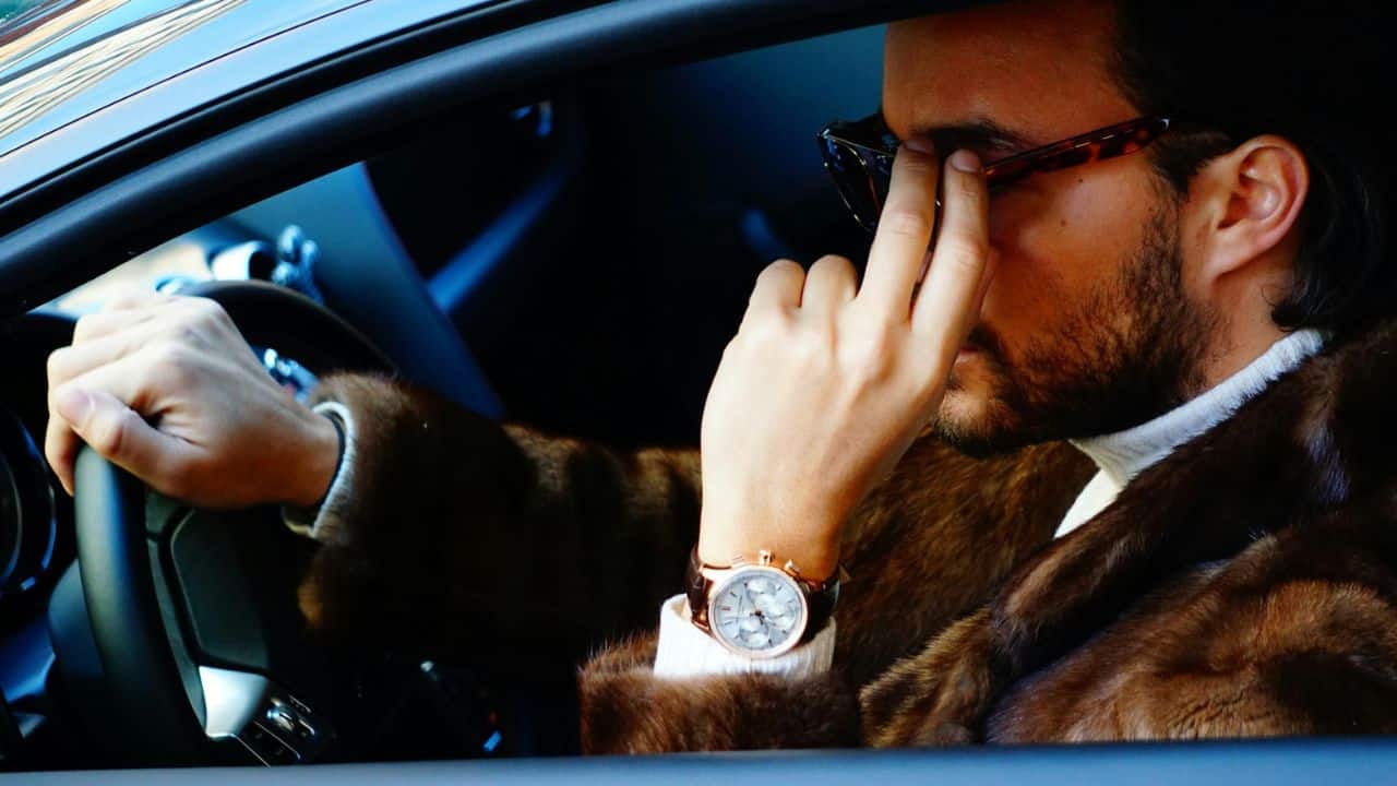 A man in a fur jacket and sunglasses is driving a car.