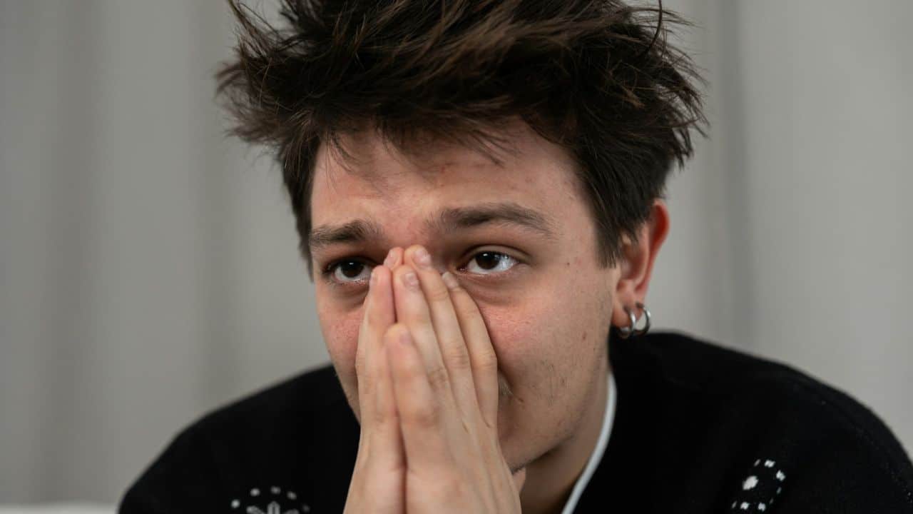 A person with brown hair and an earring sits with their hands clasped over their face.