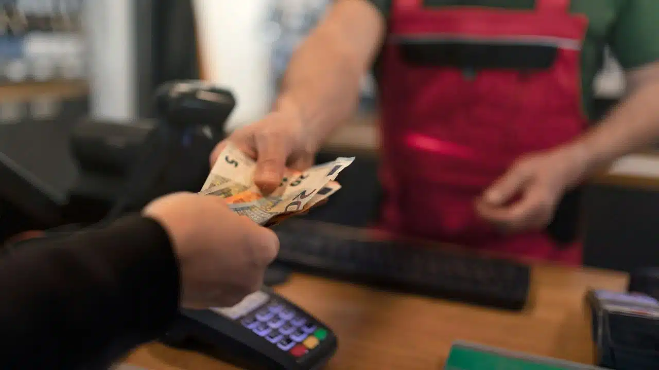 A customer's hand is giving a cashier some Euro currency notes.