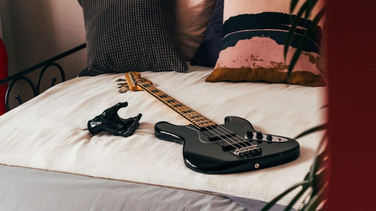 A black electric bass guitar and a black sculpture of a hand are lying on a bed.