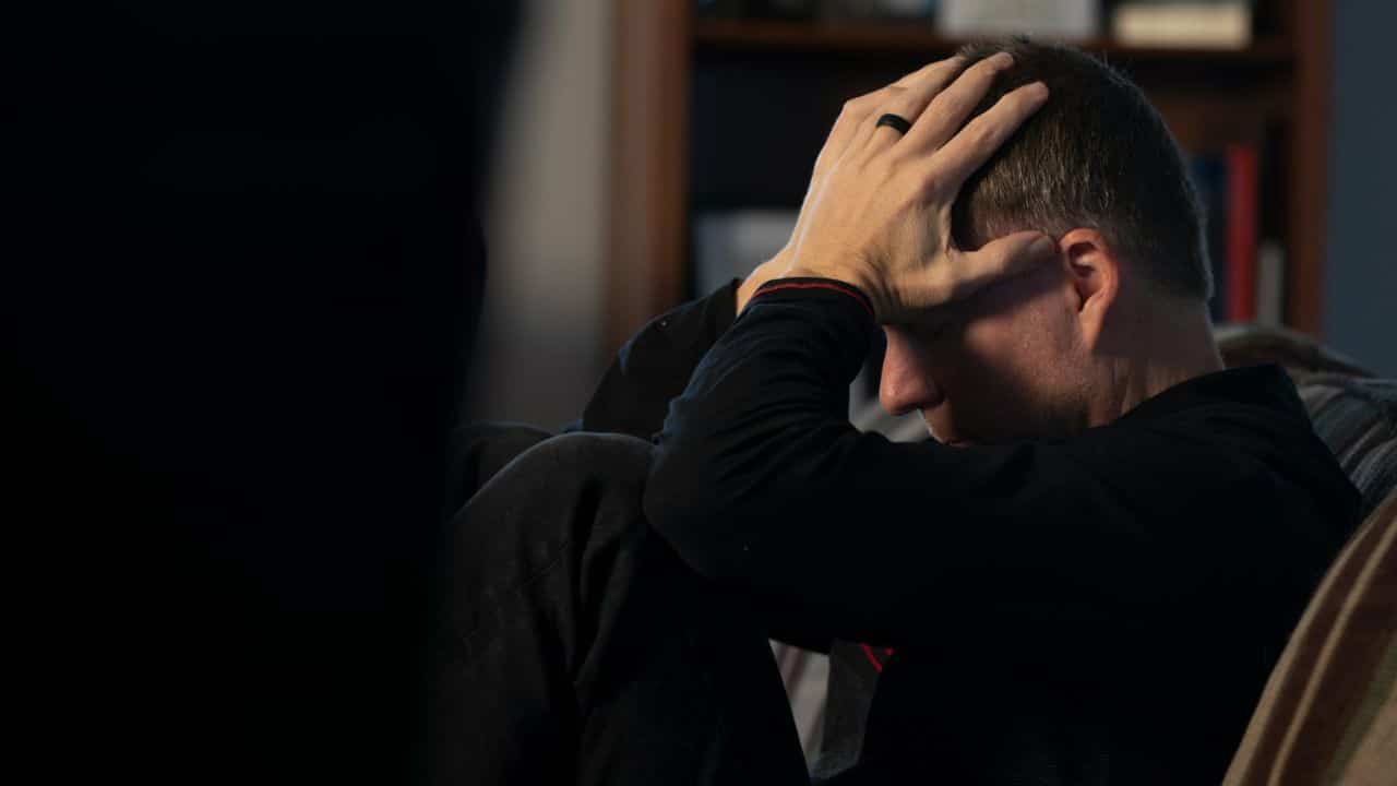 A man is sitting with his head in his hands, appearing to be in distress.