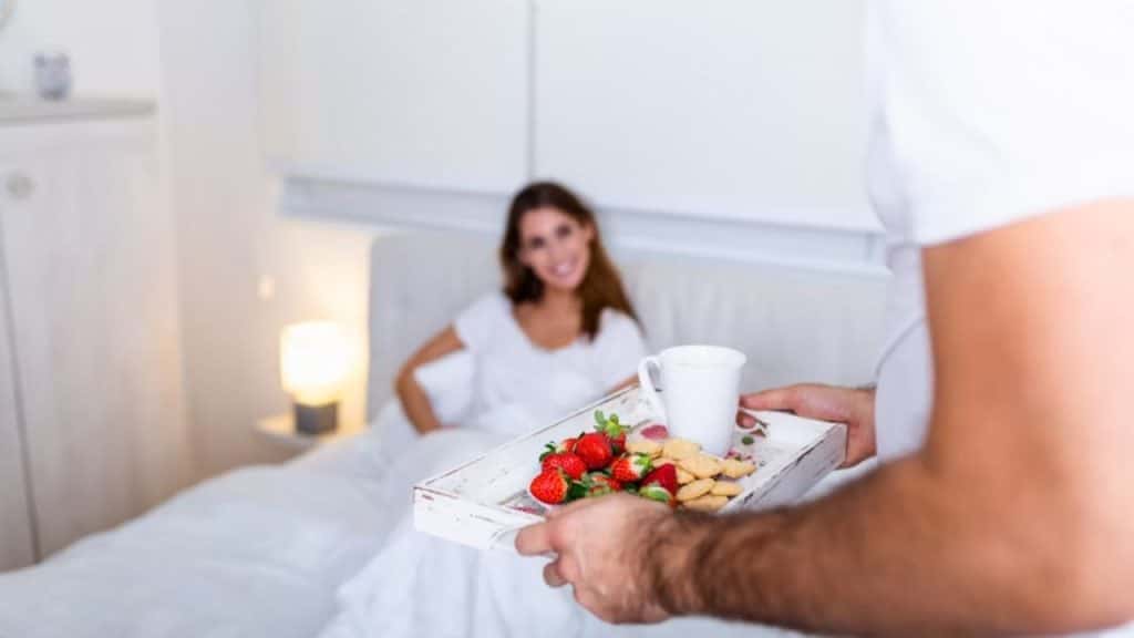 Man placing breakfast on bed for partner