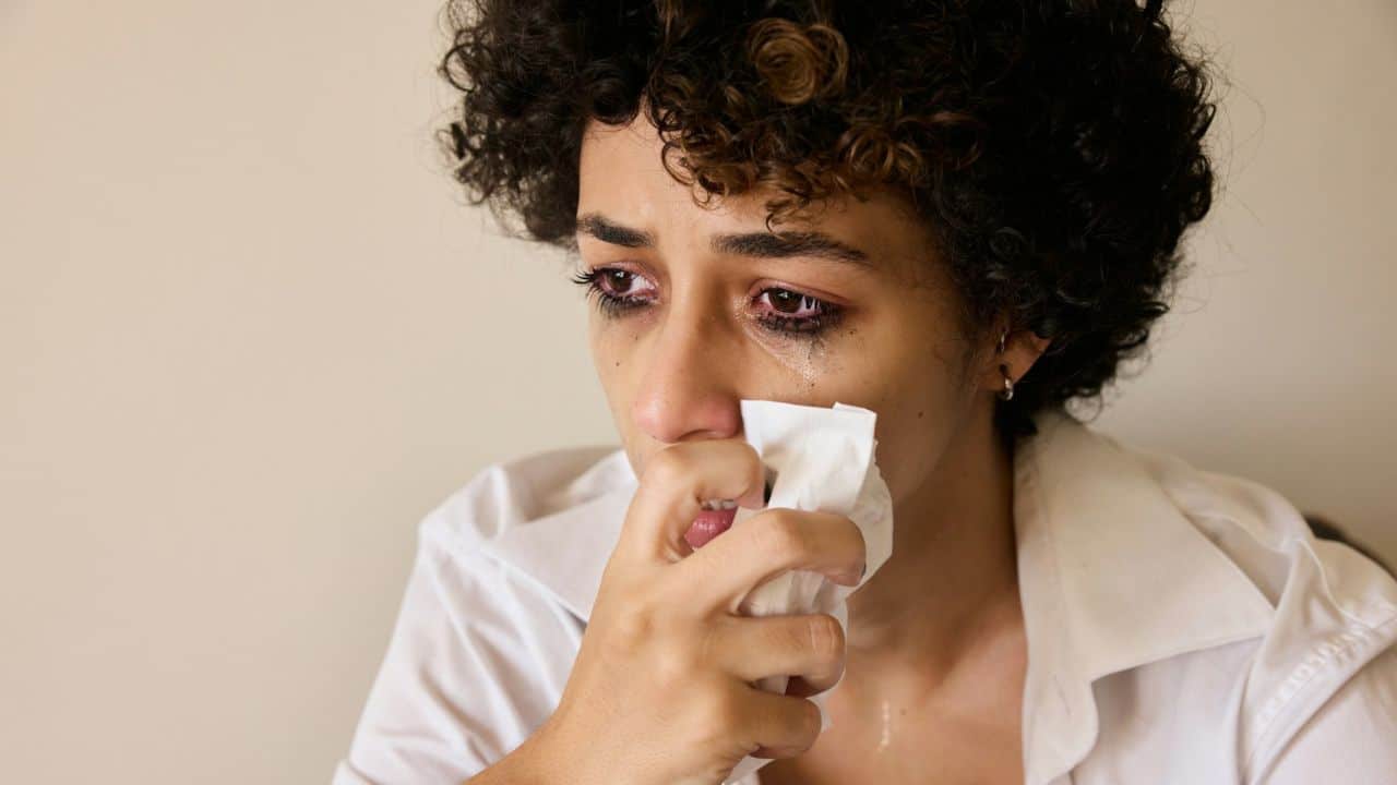 A young woman with tears streaming down her face holds a tissue to her nose.