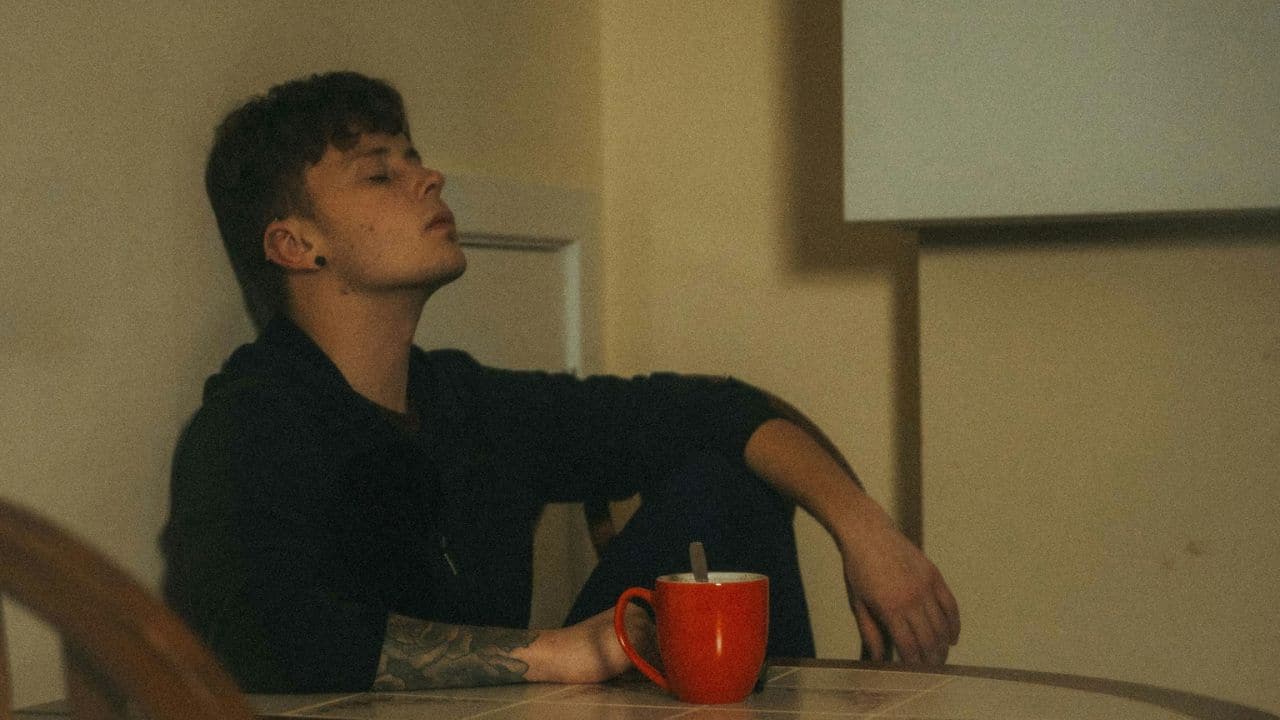 A pensive person sitting at a table with a red mug.