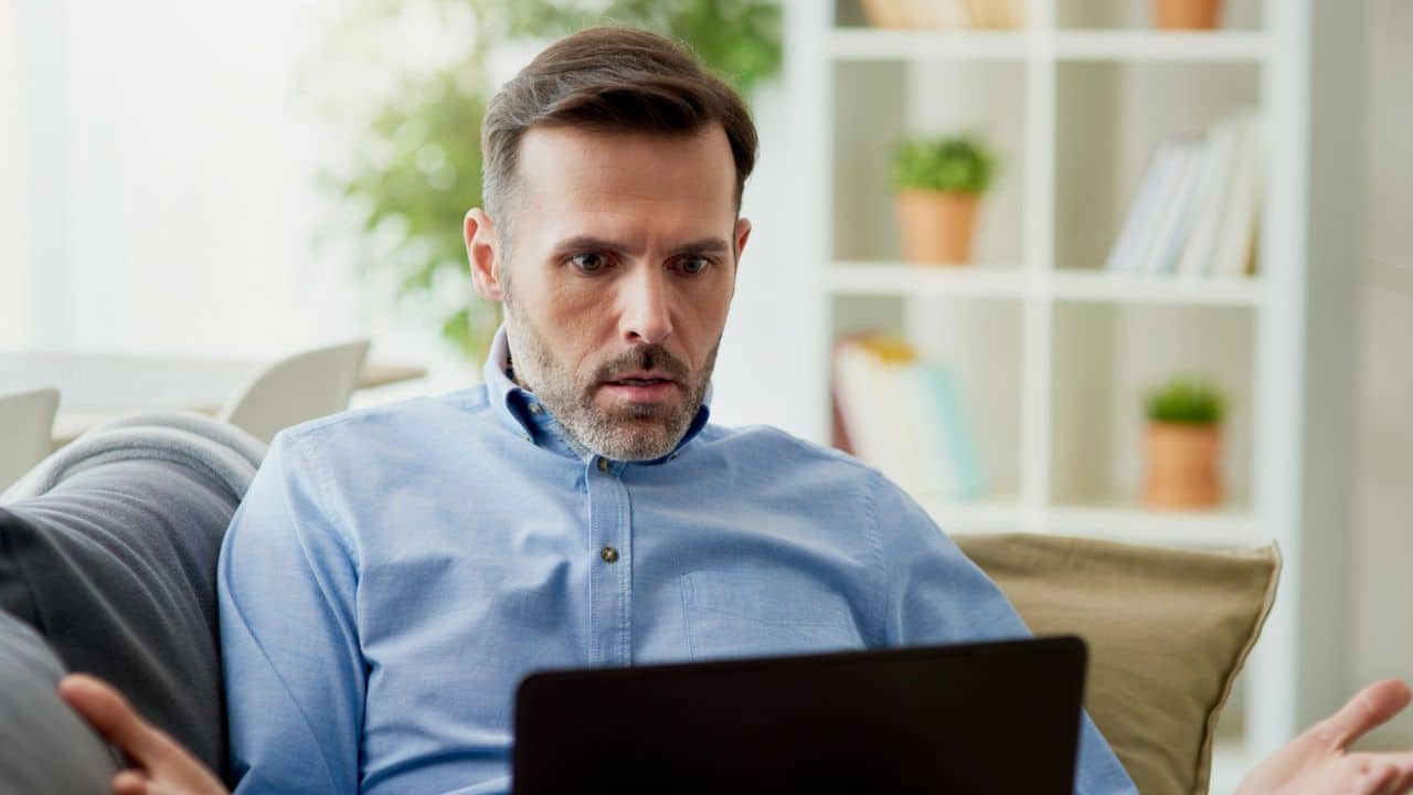 A surprised man in a blue shirt looking at a laptop.