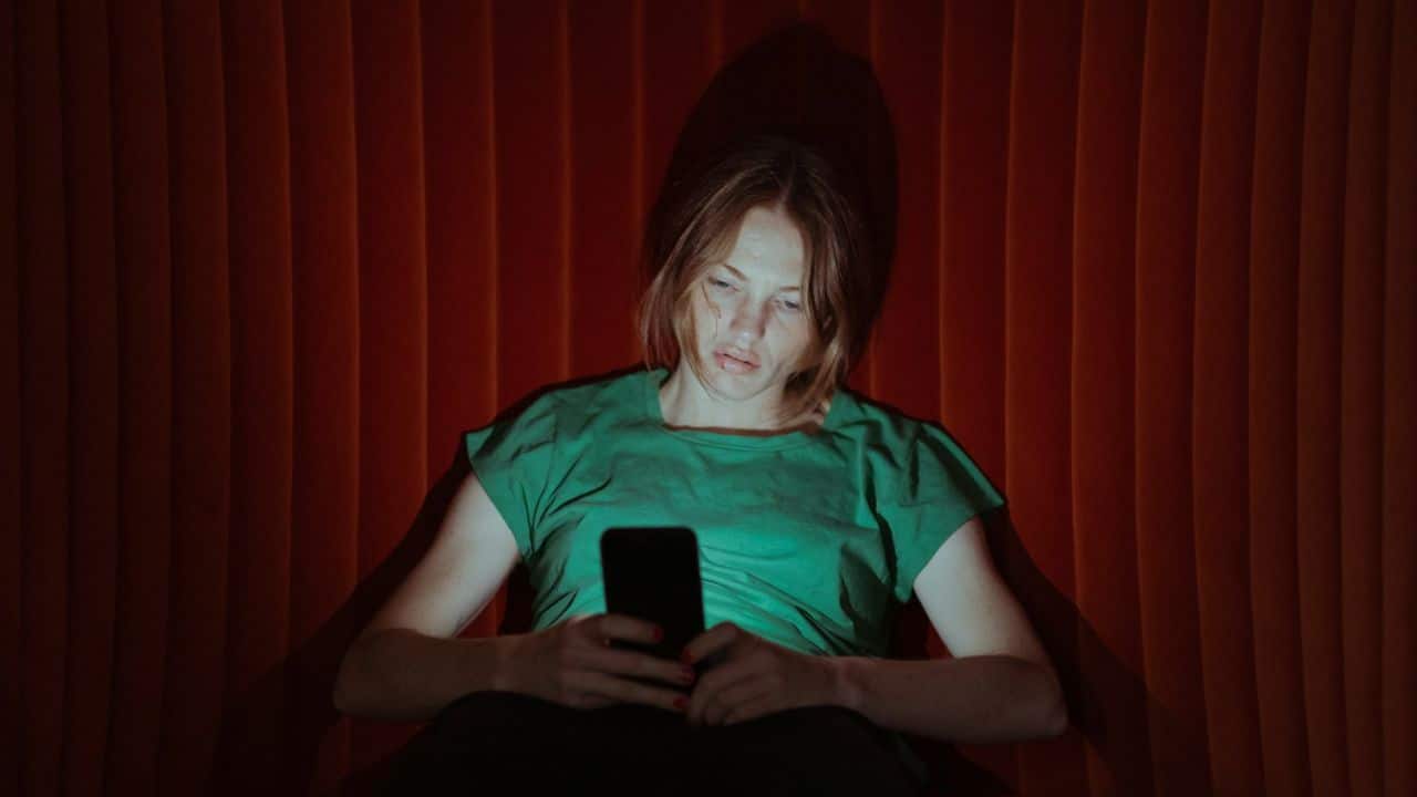 A person looking down at a phone with a serious expression, bathed in light.