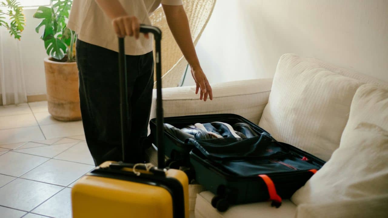 A person stands with a yellow suitcase and a black open suitcase.