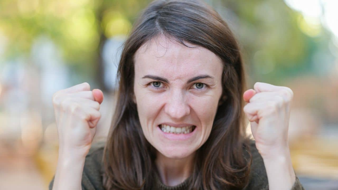 A woman with clenched fists and teeth, looking directly at the camera with a furrowed brow.