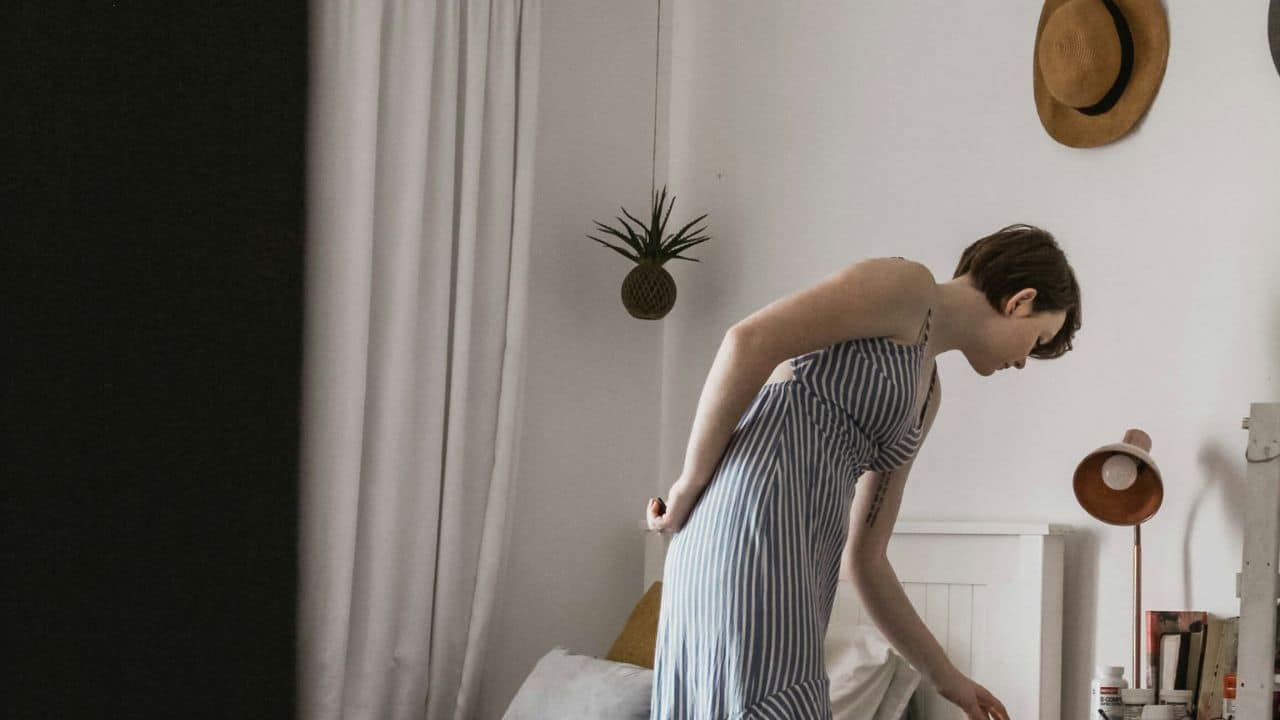 A person in a striped dress is leaning forward, with a hat on the wall behind.