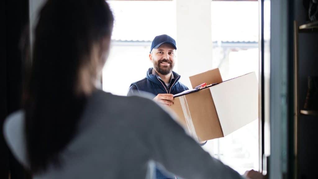 A man holds a large box, smiling at a person opening a door.