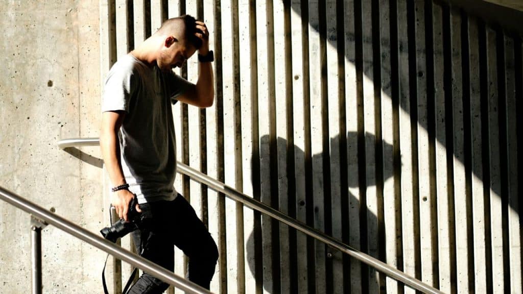A man holds his head and looks down as he walks down a flight of stairs.