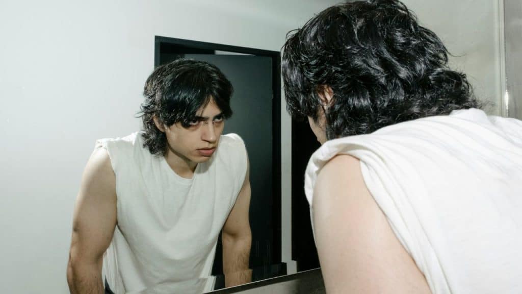 A worried man stares intensely at his reflection in a bathroom mirror.