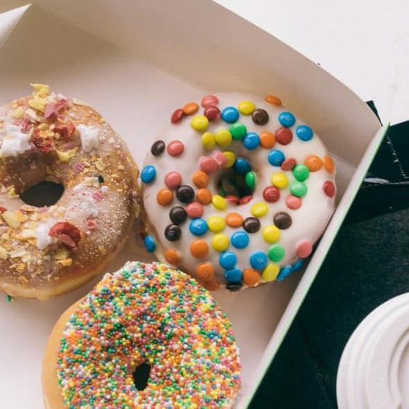 A box with three colorful donuts and a coffee cup.