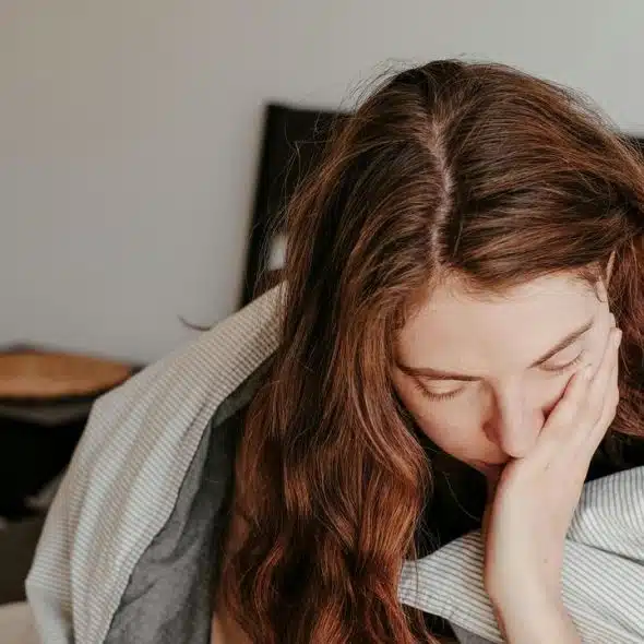 An exhausted woman sitting on a bed with her head in her hand.
