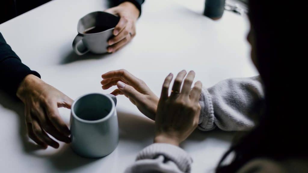 A close-up of two people holding coffee mugs at a table.