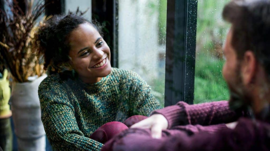 A woman smiling at someone by a rainy window.