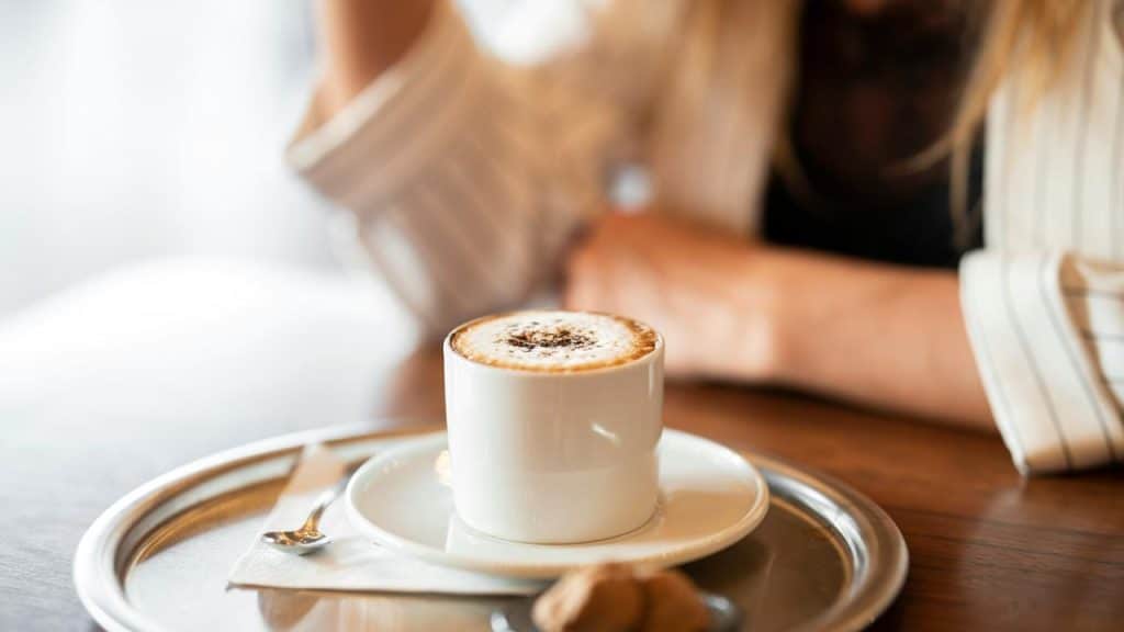 A cup of cappuccino on a tray with a spoon and cookies.
