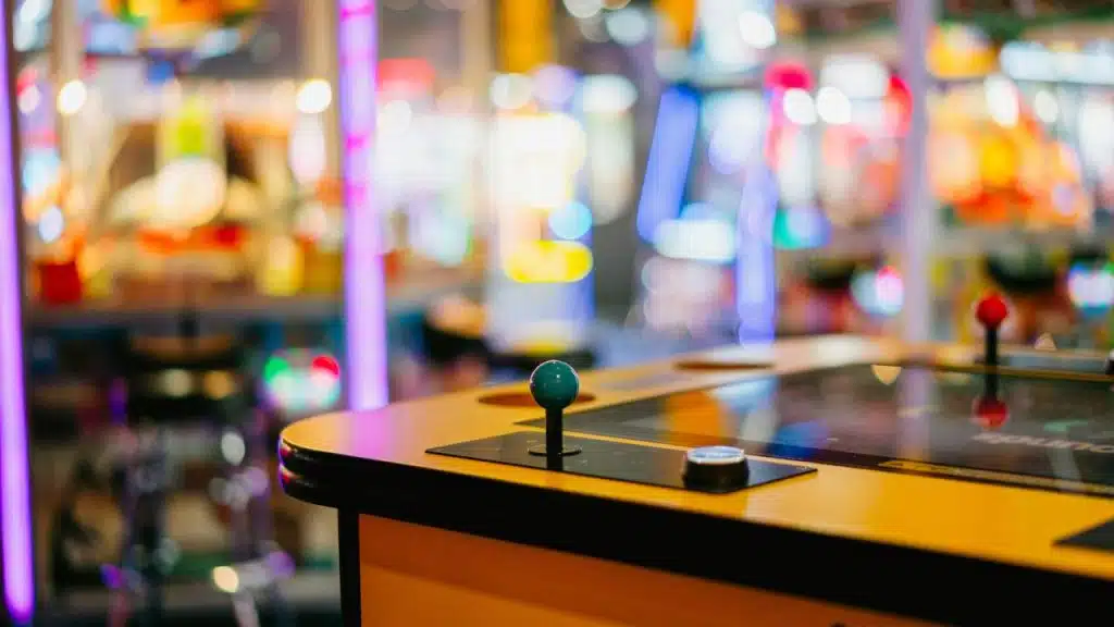 A close-up of an arcade game joystick with colorful lights in the background.