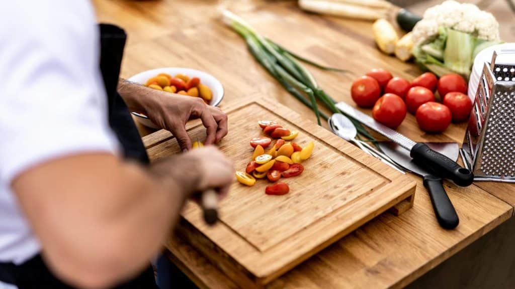 A person chopping cherry tomatoes on a wooden cutting board.