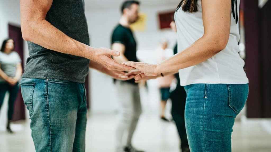 A couple holding hands while learning to dance in a group class.