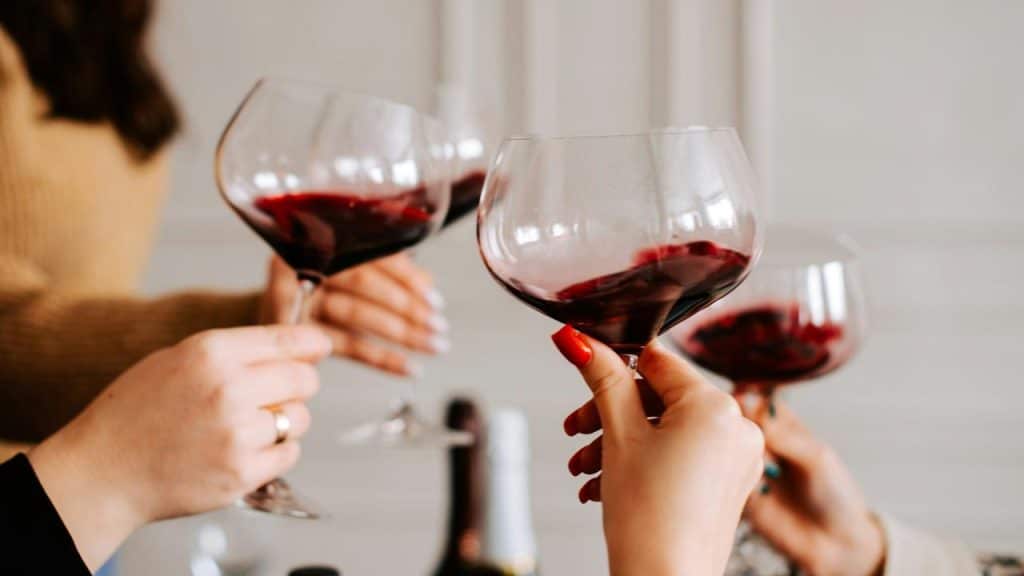 A close-up of people clinking wine glasses with red wine.