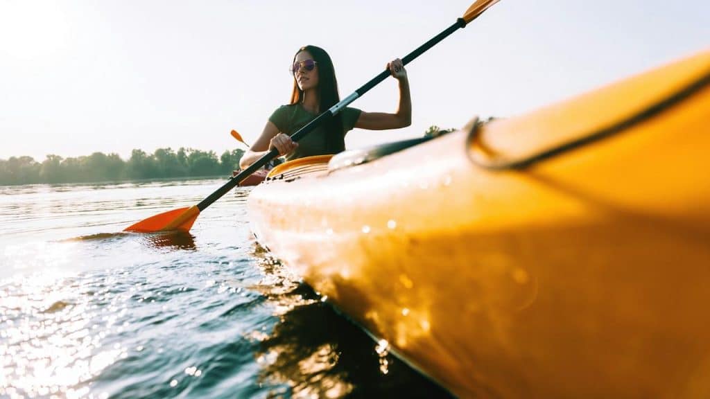 A woman kayaking on a calm lake under the sun.