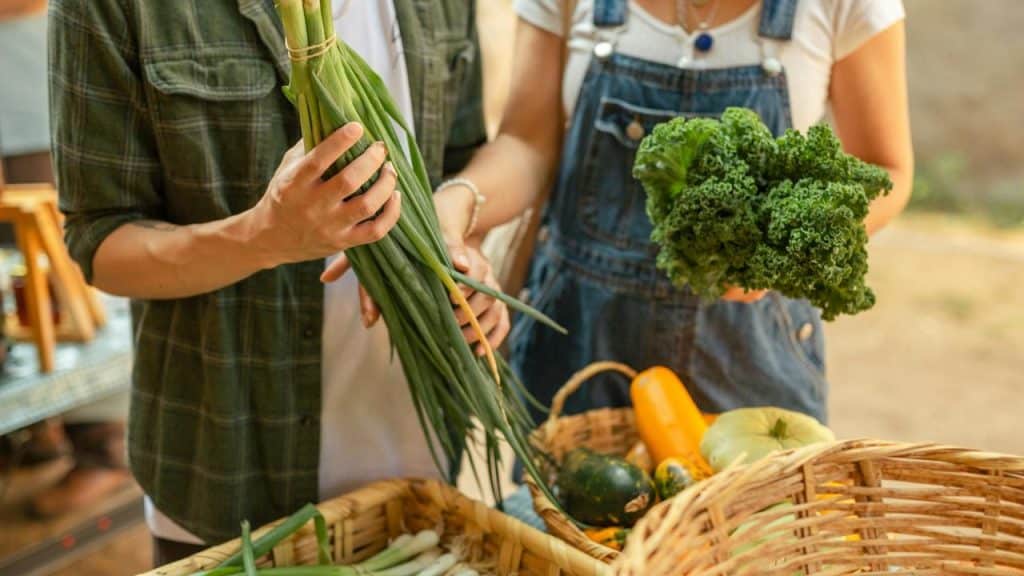 A close-up of two people holding fresh vegetables at a market.