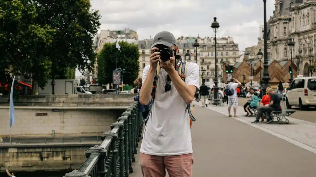 A man taking a photo on a city street with buildings in the background.
