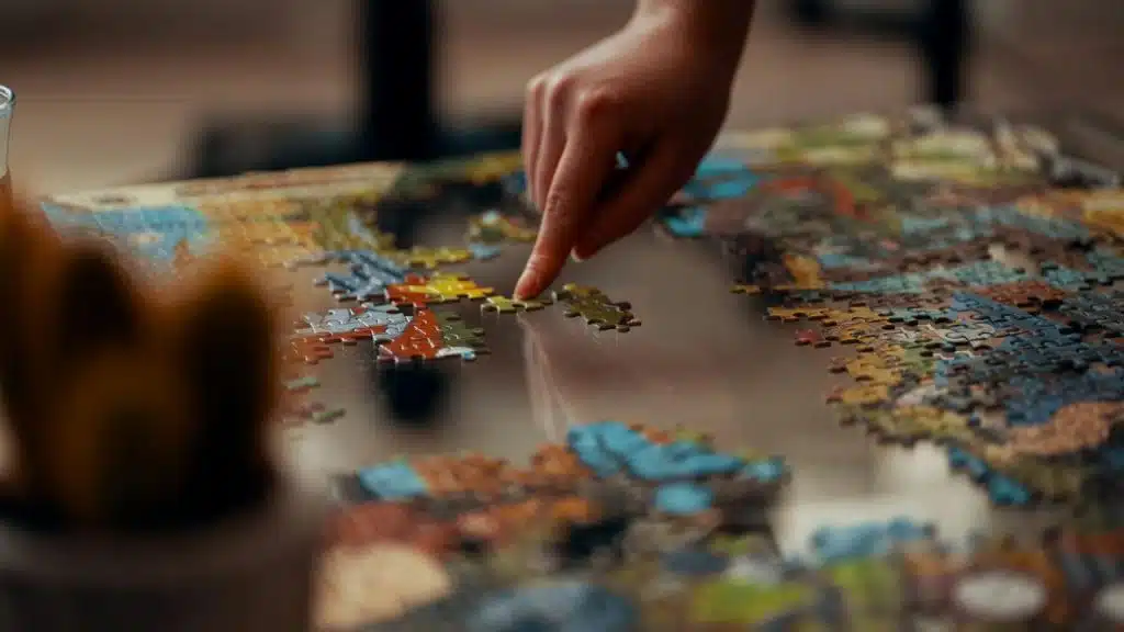 A person assembling a colorful jigsaw puzzle on a table.