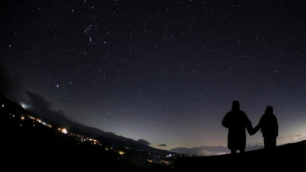 A couple holding hands while stargazing under a clear night sky.