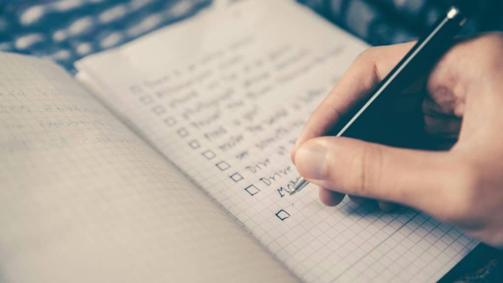 A person writing a checklist in a notebook.