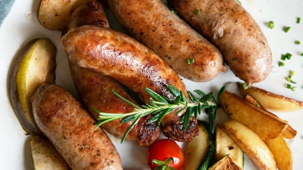 A plate of sausages with potatoes and herbs.