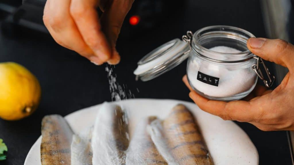A person’s hand sprinkling salt on raw fish.