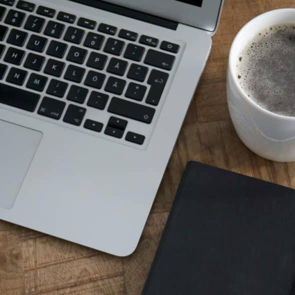 A laptop, coffee, and notebook on a table.