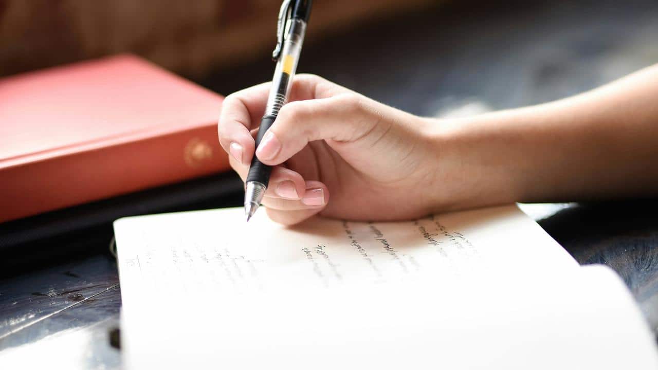A person's hand writing in a notebook with a pen.
